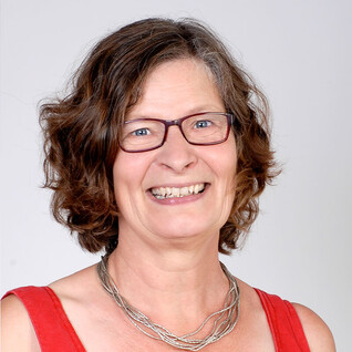 Portrait einer Frau mit kurzen Haaren, Brille und kariertem Oberteil.